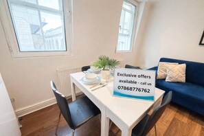 A dining area with a table set for two, a blue sofa, and a sign offering exclusive deals.