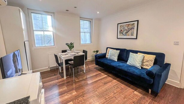 A modern living room with a blue sofa, a dining table with chairs, and a television. - 2 Bed flat w/ AC by Trafalgar square & London eye (London)