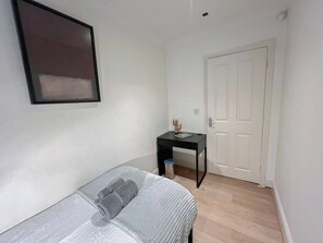 A small, sparsely furnished room with a bed, a desk, and a door.