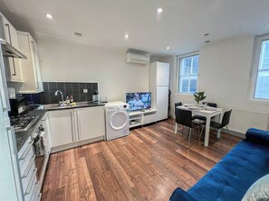 A modern kitchen with a built-in washing machine, a dining area with a table and chairs, and a blue sofa.