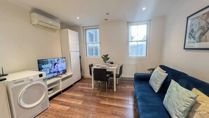 A compact living space with a dining area, a sofa, a television, and a washing machine. - 2 Bed flat w/ AC by Trafalgar square & London eye (London)