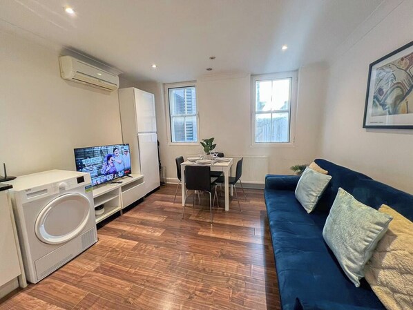A compact living space with a dining area, a sofa, a television, and a washing machine.