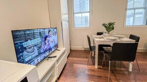 A modern living room with a flat-screen TV, a dining area with a table set for two, and a large window providing natural light. - 2 Bed flat w/ AC by Trafalgar square & London eye (London)