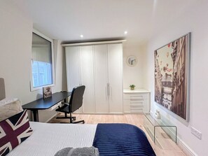 A bedroom with a bed, a desk, a chair, a wardrobe, and a painting on the wall.