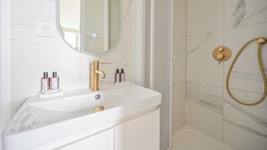 A bathroom with a white sink, gold faucet, and a shower with a gold showerhead.