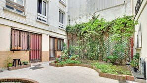 A courtyard with a tiled floor, a small water feature, potted plants, and a brick border.