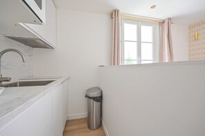 Una cocina moderna con armarios blancos, un lavamanos de acero inoxidable y un bote de basura.