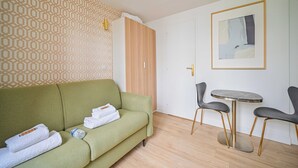 A room with a green sofa, a small round table with two chairs, a wooden wardrobe, and a patterned wall.