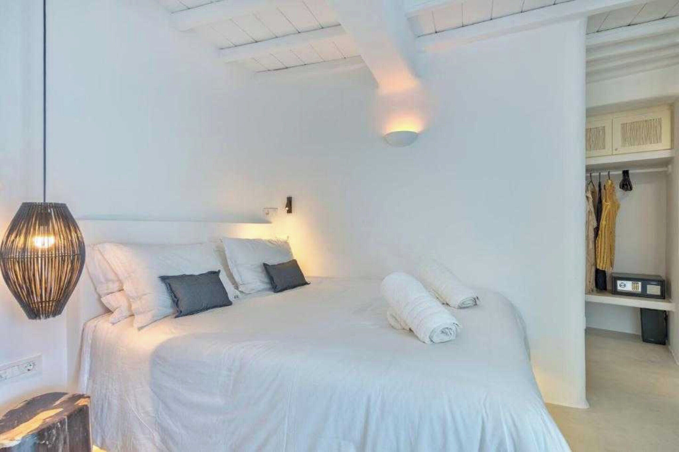 A bedroom with a bed, pillows, a rolled towel, a lamp, and a wardrobe.