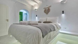 A modern bedroom with a large bed, white walls, and a unique ceiling design. - Cosy Flat on the Shore - 1bd/2p - Mykonos (Mykonos)