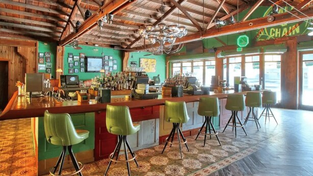 Una zona de bar con vigas de madera, paredes verdes y suelo estampado.