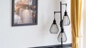 A room with a framed floral artwork on the wall, a black floor lamp, a wooden side table, and a yellow curtain. - Modern 2-Bedroom Southsea Flat with Free Parking (Portsmouth)