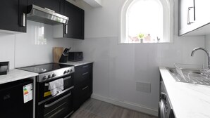 A modern kitchen with black cabinets, a stainless steel range hood, a built-in oven, a dishwasher, and a window with a view of the outside. - Modern 2-Bedroom Southsea Flat with Free Parking (Portsmouth)