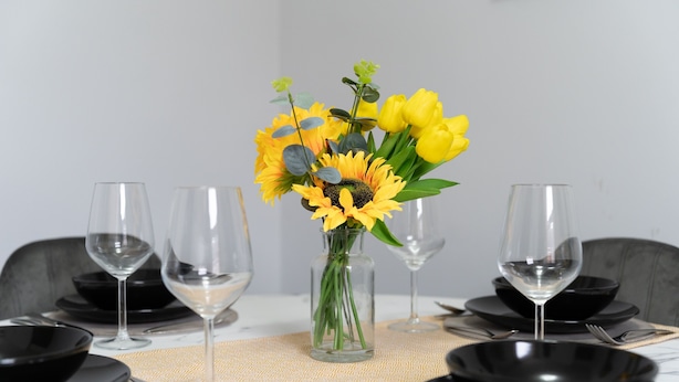 A dining table set with black plates, clear wine glasses, and a vase with yellow flowers. - Modern 2-Bedroom Southsea Flat with Free Parking (Portsmouth)