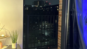Ein Balkon mit Blick auf eine nächtliche Stadtlandschaft, einem Blumentopf und einer Kerze auf einem Tisch.