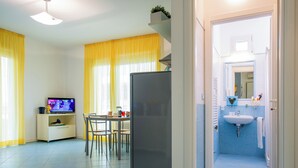 Un espace de vie compact comprenant un coin repas, une cuisine équipée d’un réfrigérateur, et une salle de bain avec un lavabo et un miroir.