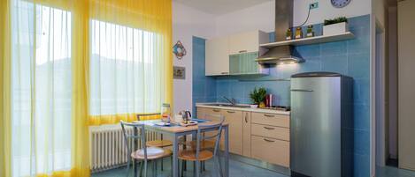 A compact kitchen with a dining area, featuring a refrigerator, stove, and a clock on the wall.