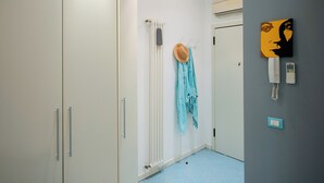 Un couloir avec une armoire blanche, un radiateur, un chapeau, une écharpe et un téléphone fixé au mur.