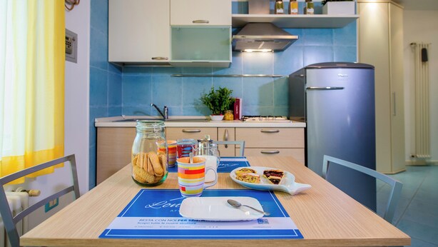 Une cuisine avec un mur recouvert de carreaux bleus, un réfrigérateur en acier inoxydable et une table à manger où sont disposés une assiette de nourriture, une tasse et un bocal de biscuits.