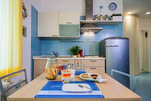 Eine Küche mit blauen Fliesen an der Spritzschutzwand, einem Edelstahlkühlschrank und einem Esstisch, gedeckt mit einem Teller Essen, einer Tasse und einem Glas Kekse.