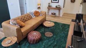 Un soggiorno con un divano marrone, due tavolini rotondi in legno, un tappeto shag verde e un mobile TV con un telecomando.