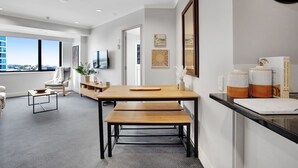 Une chambre d’hôtel moderne dotée d’une grande fenêtre, d’un coin repas avec une table et un banc en bois, et d’un comptoir de cuisine agrémenté d’objets décoratifs.
