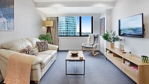 Un salon moderne comprenant un canapé, un fauteuil, une table basse et un téléviseur posé sur un meuble en bois.