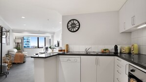Une cuisine moderne avec des meubles blancs, une horloge noire et une vue sur la ville grâce à de grandes fenêtres.