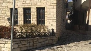 A stone-paved street with a stone building featuring a metal fence and a window. - Through Mangalem (Berat)