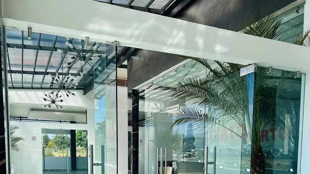 Un vestíbulo moderno con puertas de vidrio, piso de mármol y una gran planta en maceta.