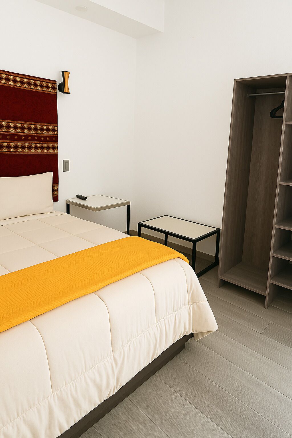 A hotel room with a bed, bedside table, and a wardrobe.