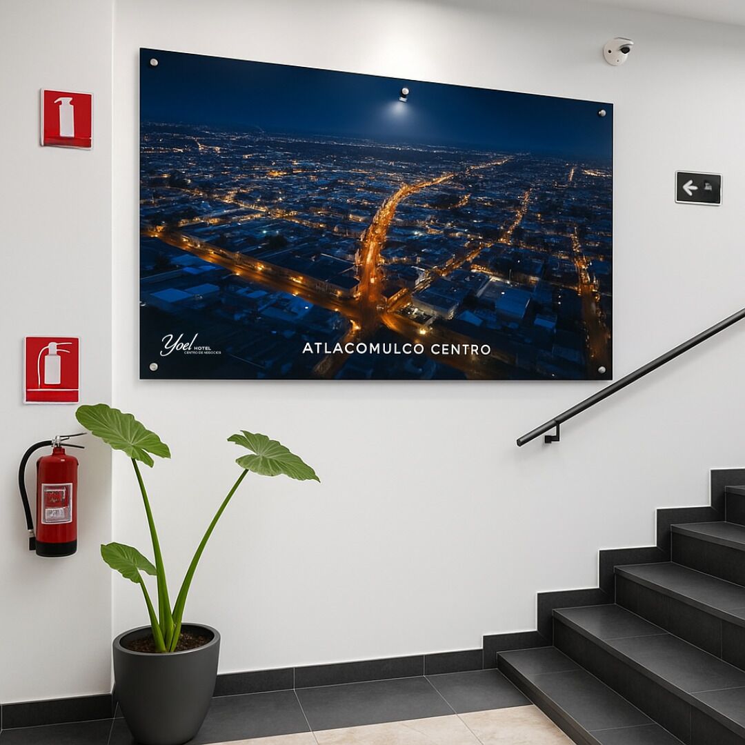 A framed cityscape poster of ATLACOMULCO CENTRO, a fire extinguisher, and a potted plant in a hallway.