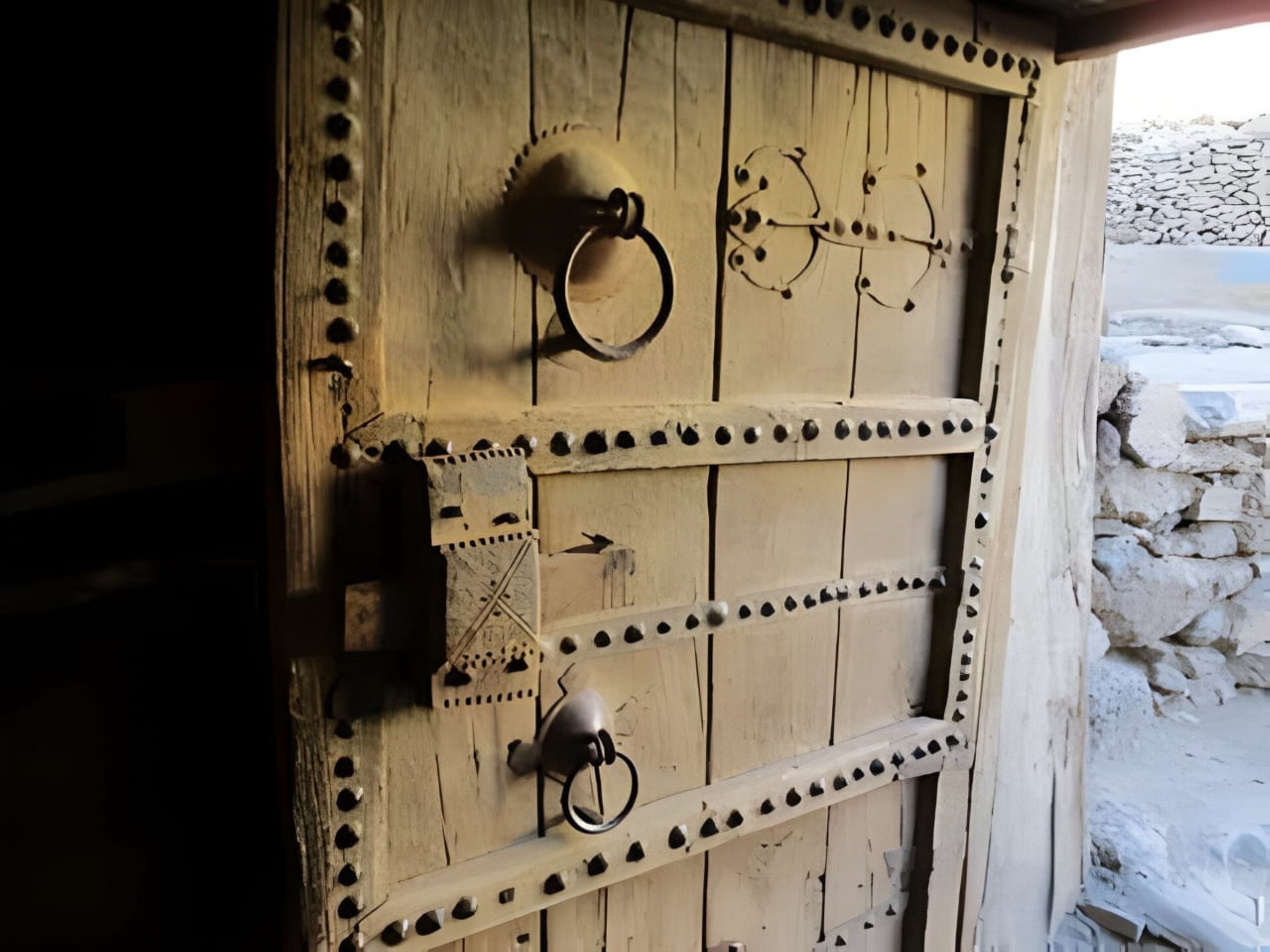 Una puerta de madera rústica con refuerzos metálicos y un tirador de metal en forma de anillo.