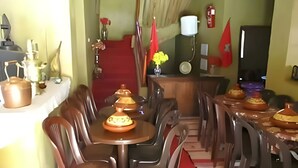 A dining area with a long table, plastic chairs, and a red carpet. - dar awlim (Imilmaiss)