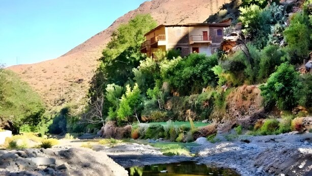 A rustic building with a balcony, surrounded by lush greenery and a rocky hillside. - dar awlim (Imilmaiss)
