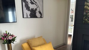 A compact living space with a sofa bed, a flat-screen TV, a framed abstract painting, and a small table with a vase of flowers. - Luxury Lane: Pet & Family Haven Near ASU & GF Base - Stock Show 7 mi - No Stairs (San Angelo)