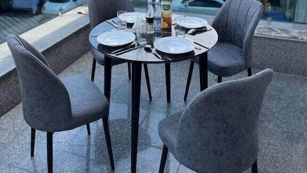 A rooftop terrace with a table set for dining, surrounded by chairs, overlooking a cityscape with buildings and parked cars. - Annur Boutique Hotel (Samarkand)