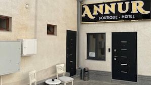 An exterior of a building with a sign reading "ANNUR BOUTIQUE - HOTEL". There are two white chairs and a small round table in front of the entrance. - Annur Boutique Hotel (Samarkand)