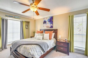 Un dormitorio con cama, mesita de noche, ventilador de techo y ventana con persianas.