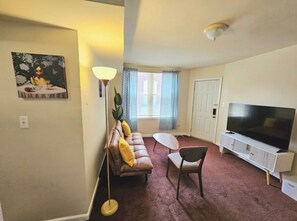 Un salon avec un canapé, un fauteuil, une télévision et un tableau accroché au mur.