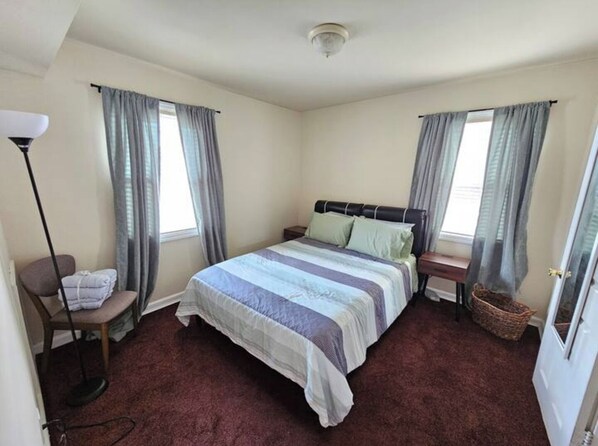 Une chambre à coucher avec un lit, deux tables de chevet, une lampe et une fenêtre avec des rideaux.