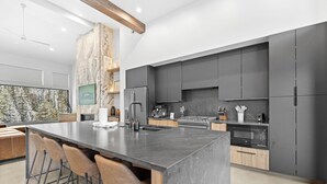 A modern kitchen with a large island, dark cabinetry, and a stone accent wall. - Luxury Townhome, Steps From Ski Lifts w/ Private Hot Tub & Mountain Views! (Keystone)