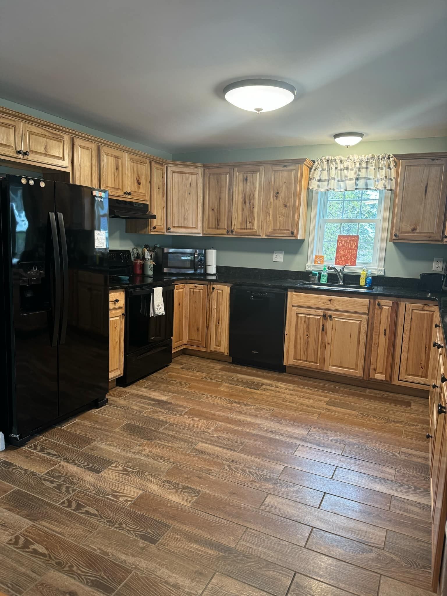 Una cocina con armarios de madera, un refrigerador negro, un microondas y un lavavajillas.