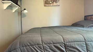 Un dormitorio con cama, televisión montada en la pared y lámpara de pared.