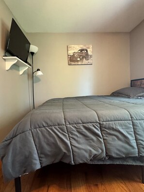 A bedroom with a bed, a mounted TV, and a wall-mounted lamp. - Northern Maine Getaway-Direct Trail Access (Fort Fairfield)