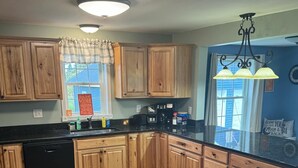 A kitchen with wooden cabinets, a black dishwasher, and a window with a view. - Northern Maine Getaway-Direct Trail Access (Fort Fairfield)