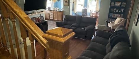 Una sala de estar con una escalera de madera, un televisor de pantalla plana, un sofá y una estantería.