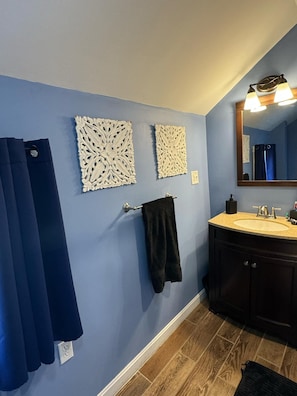 A bathroom with blue walls, a wooden floor, a sink with a mirror, and decorative wall panels. - Northern Maine Getaway-Direct Trail Access (Fort Fairfield)