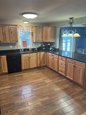 A kitchen with wooden cabinets, a dishwasher, and a countertop with various appliances. - Northern Maine Adventure (Fort Fairfield)