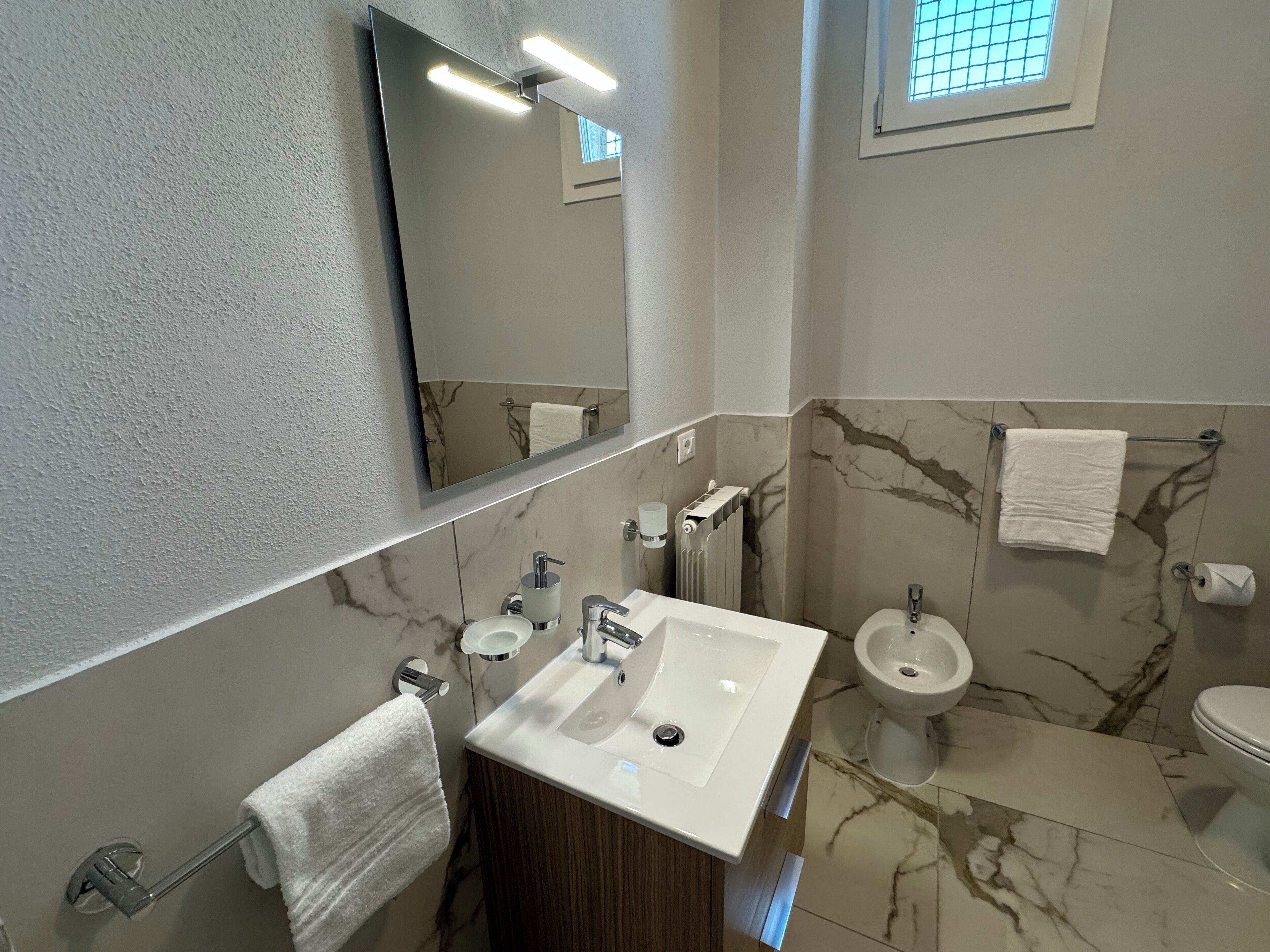 Une salle de bain avec un sol en marbre, un grand miroir, un lavabo, des toilettes et un bidet.